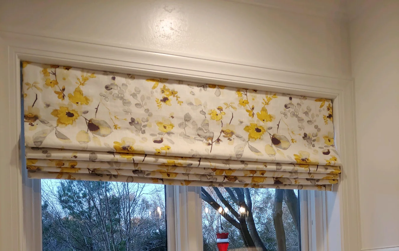 Floral fabric Roman shade with visible pleats above a kitchen window